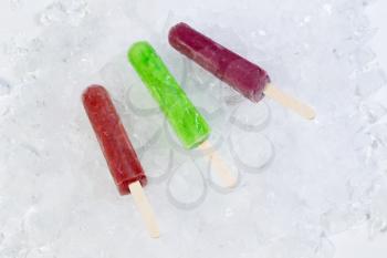 Horizontal view of colorful frozen fruit popsicles on shaved ice