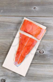 Vertical top view of raw red salmon, skin side down, on maple wood grilling plank with rustic wooden boards underneath