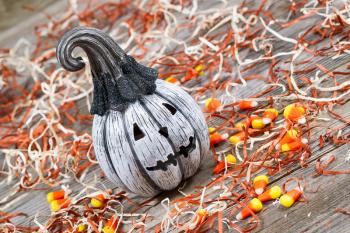 Horizontal angled image of a scary black and white pumpkin surround by shredded paper, candy and rustic wooden boards 