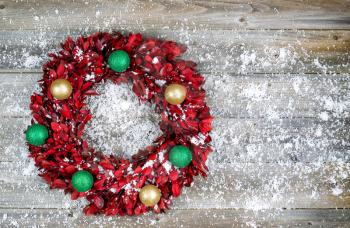 Top view of wreath consisting of real tree leaves and Christmas ornaments with snow on rustic wood 