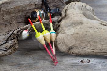 Closeup horizontal image of fishing objects consisting of floats, reel, single lure all resting against aged driftwood 