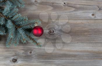 Horizontal image of a single red Christmas ornament hanging from a real Blue Spruce tree branch placed on rustic wooden boards