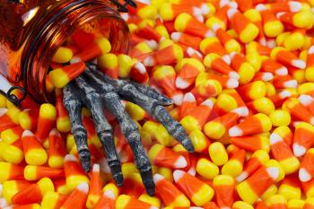 Closeup image of a scary hand coming out of jar into pile of candy corn