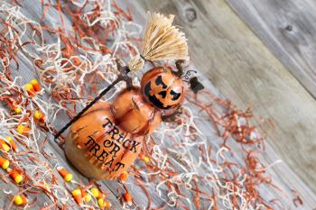 Horizontal angled image of a scary orange pumpkin figure holding straw broom placed on rustic wooden boards 