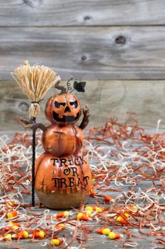 Vertical image of a scary orange pumpkin figure holding straw broom placed on rustic wooden boards 
