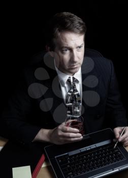 Vertical image of business man, looking at computer screen, working late with black background 