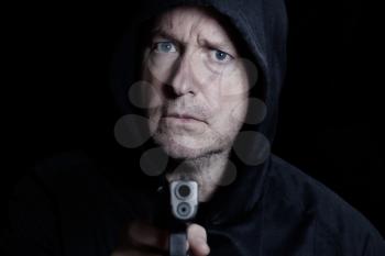 Closeup front view of mature man, looking forward, with gun in hand on black background 