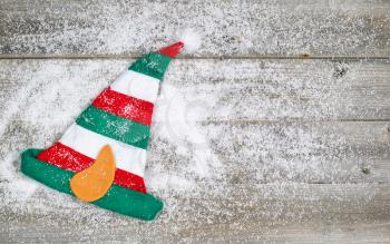 Horizontal image of Christmas elf stocking hat on rustic wooden boards covered with snow 

