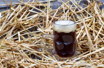 Horizontal image of a glass stein filled with dark draft stout beer on rustic wood and straw 
