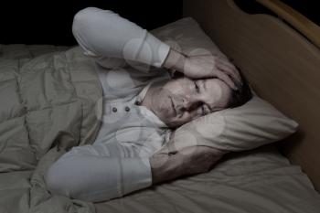 Horizontal image of sick mature man, holding his head, while in bed 