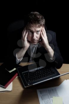 Vertical image of a tired business man working late into the night with black background 