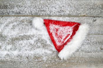 Horizontal image of Christmas Santa hat, covered with snow, on rustic wooden boards