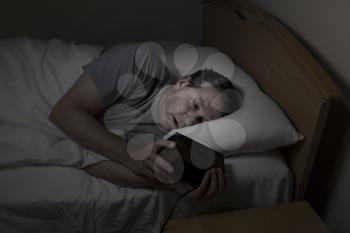 Mature man, eyes open with both hands on alarm clock while checking time, cannot sleep at night from insomnia