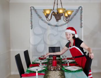 Young teenage girl, dressed in Santa outfit, setting dining room table for the holidays 
