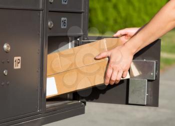 Horizontal image of female hands taking large package out of postal mailbox with green grass and sidewalk in background 