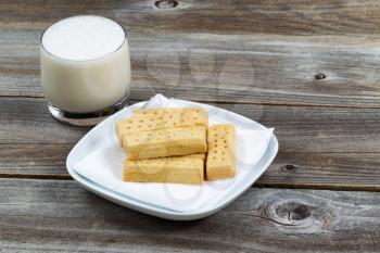 horizontal image of butter cookies, on white napkin and plate, and a full glass of rich milk with rustic wood underneath