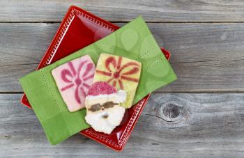 Top view of Christmas sugar cookies on green cloth napkin and red plate with rustic wood underneath 