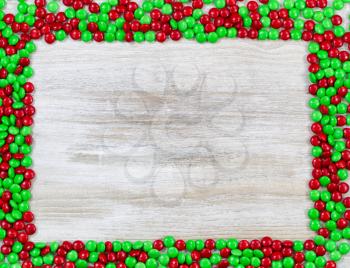 Top view of little red and green candies forming a border on rustic wooden boards 