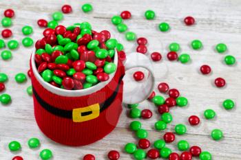 Close up of a holiday red mug spilling of sweet candy onto rustic white wooden boards 
