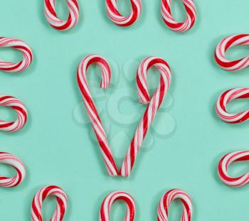 Image of red and white stripped candy canes on a solid light green background. Pattern of a heart shape in center of frame with canes in and out of the frame to form even border. 
