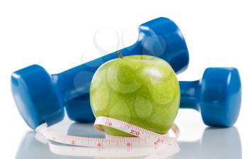 Close up of a pristine green apple, two dumbbells, measuring tape isolated on white with reflection. 