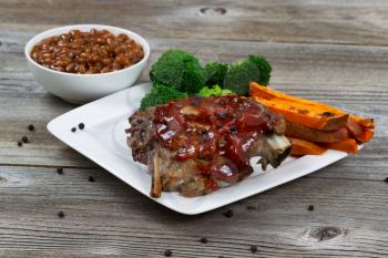 Barbecued spare ribs with yam French fries, broccoli and baked beans on rustic wooden table. 