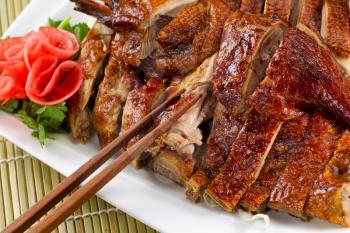 Chinese roasted duck dish with radish decoration on side of white plate