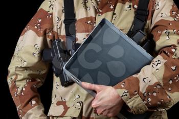 Close up horizontal image of laptop computer with armed male soldier holding it while on black background. 