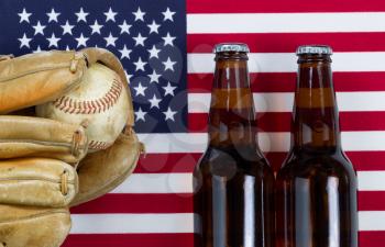 Close up image of worn leather mitt, used baseball and full beer bottles with United States of America flag in background. 