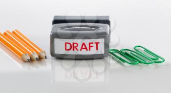 Draft stamp, paper clips and pencils on glass with white background and reflection