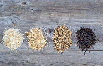 Top view of various rice types each within an individual pile on rustic wood