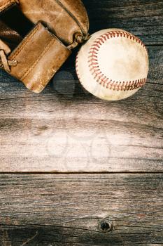 Vintage concept of an old baseball and weathered leather mitt on rustic wood. Format in vertical layout. 