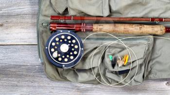 Antique fly fishing reel and rod with vest and flies on rustic wood. Layout in horizontal format.