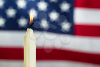 Close up image of a single white candle and glowing flame with United States of America flag in background. Fourth of July holiday concept. 