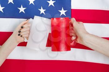 Close up image of both female and male hands holding large plastic drinking mugs with United States of America flag in background. Fourth of July holiday concept. 