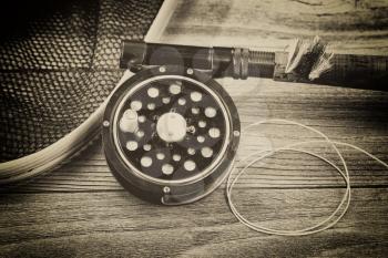 Vintage concept with grain of an antique fly fishing reel, rod, landing net and artificial flies on rustic wood. Close up with layout in horizontal format.