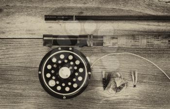 Vintage concept of an antique fly fishing reel and rod on rustic wood. Layout in horizontal format.