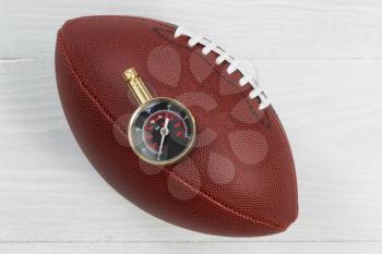 Close up of America football with air pressure gauge on top of ball with rustic white wood underneath. 