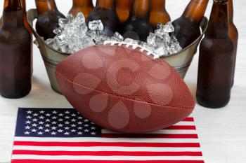 Close up of American football, ice cold beer in bucket, and flag with rustic white wood underneath. Perfect for the Fourth of July holiday. Filled frame in horizontal format. 