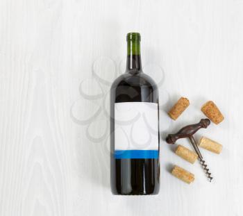 Overhead angled view of a large bottle of red wine with an antique corkscrew with old corks on white wood. 