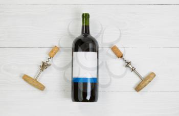 Large, unopened, bottle of red wine with vintage corkscrew openers on white wooden boards. 