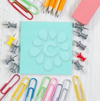 Close up image of school supplies consisting of the following: paper, tacks, paper clips, pencils and eraser on white wood. 