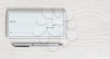 Close up of blank checkbook and silver pen on white wooden desktop. Layout in horizontal format.