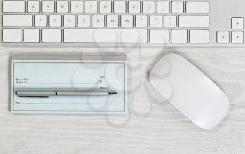 Image of partial keyboard, blank checkbook, silver pen and mouse on white desktop. Layout in horizontal format.