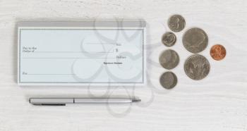 Close up of blank checkbook, silver pen and coins on white wooden desktop. Layout in horizontal format.