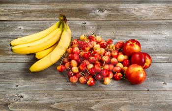 Fresh ripe fruit consisting of cherries, peaches and bananas on rustic wood. 
