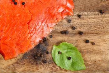 Close up of thinly sliced cold smoked red salmon on wooden server board with basil leafs and black peppercorn.