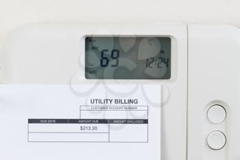 Close up of home heating thermostat with partial utility bill on wall.