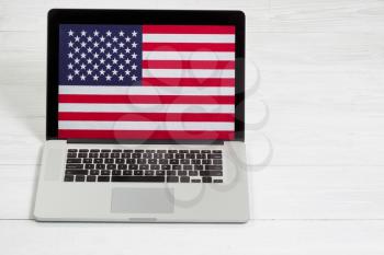Mobile computer, United States of America flag on display screen, on white desktop. Concept of USA computer unsecured. 