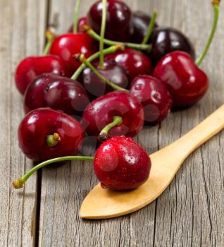 Close up image freshly picked whole cherries, focus on cherry in spoon, on rustic wood. 